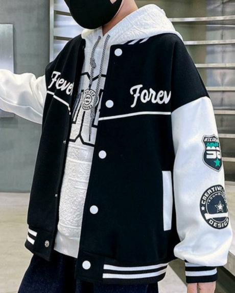 Un garçon debout qui porte un blouson teddy noir aux manches blanches.
