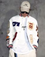 Blouson blanc de style baseball avec broderie multi-lettres pour homme porté par un homme avec des lunettes et une casquette sur fond gris