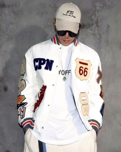 Blouson blanc de style baseball avec broderie multi-lettres pour homme porté par un homme avec des lunettes et une casquette sur fond gris