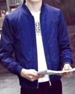 Blouson bomber homme, coupe-vent et décontracté, de couleur avec une fermeture à glissière centrale, porté par un homme avec un magazine dans les mains