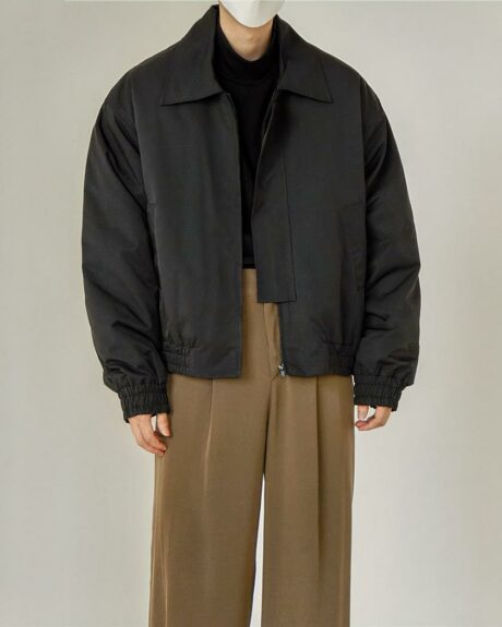 Blouson bomber homme, monochrome, style aviateur, de couleur noir, avec le col rabattu, porté par un homme debout avec un pantalon marron