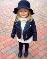 Blouson cuir fille, court, noir, style blouson perfecto, avec fermeture à glissière, porté par une fille avec un chapeau noir dans la rue