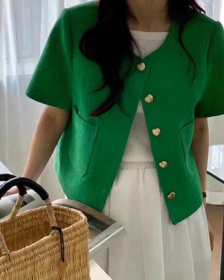 Blouson d'été, élégant pour femme, avec des boutons en forme de cœur, manches courtes, boutonnage simple, de couleur verte, porté par une femme debout, avec un panier devant elle