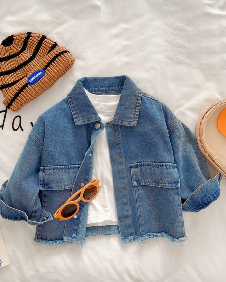Blouson en denim pour bébé fille, de couleur bleu, avec col à revers, boutonnage simple, exposé sur un lit avec un bonnet et une paire de lunette à côté