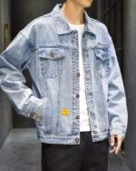 Blouson en jean homme, look streetwear, de couleur bleu, avec poche au niveau de la poitrine et 2 sur les côtés, porté par un homme debout avec la main dans la poche