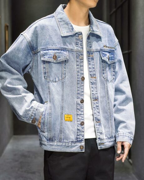 Blouson en jean homme, look streetwear, de couleur bleu, avec poche au niveau de la poitrine et 2 sur les côtés, porté par un homme debout avec la main dans la poche