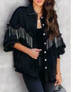 Une femme portant une veste en jean noir à franges, elle se tient debout sur un mur gris.