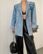 Blouson en jean vintage long et ample pour femme porté par une femme avec un sac à main sur fond blanc