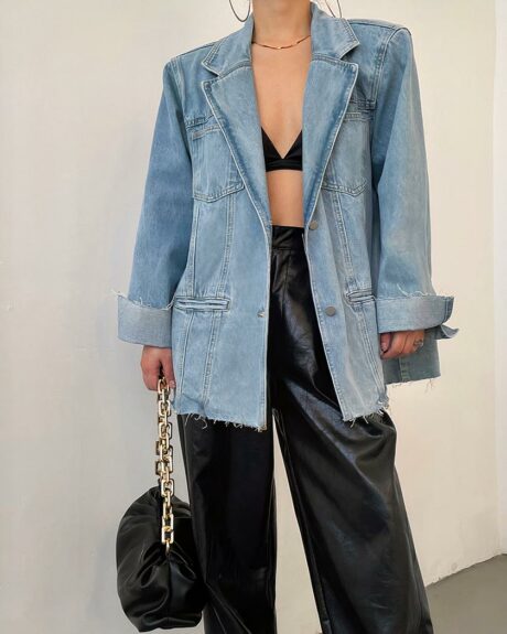 Blouson en jean vintage long et ample pour femme porté par une femme avec un sac à main sur fond blanc