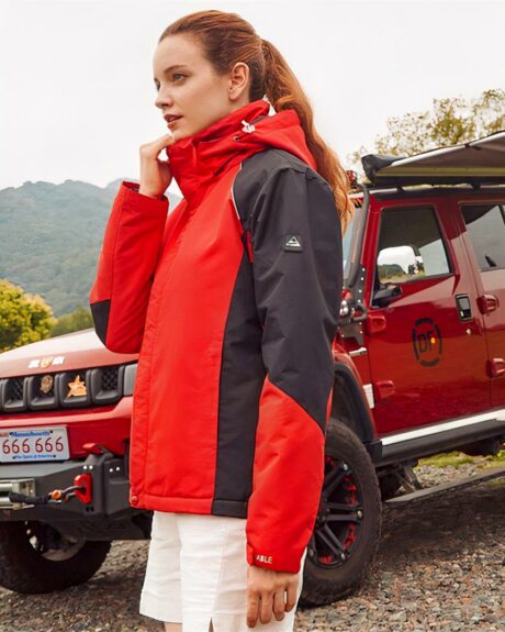 Blouson imperméable coupe-vent de randonnée pour femme sur une femme dans la nature sur fond de collines et une voiture rouge