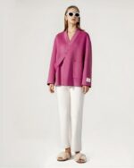Blouson laine femme, avec boucle oblique, boutonnage simple, de couleur rose, porté par une femme debout avec un pantalon blanc