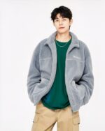 Blouson polaire homme, a col rabattu, matière style laine d'agneau, de couleur gris, porté par un homme avec les mains dans les poches