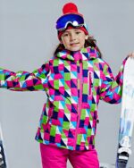 Blouson ski fille à capuche couleurs flashy porté par une jeune fille qui tient des skis dans chaque main