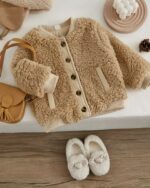 Un blouson marron à fourrure posé sur un fond blanc avec d'autres accessoires pour fille.