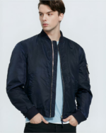 Un homme qui porte un blouson bomber bleu foncé avec les mains dans ses poches de pantalon noir.