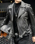 Un homme portant un blouson de motard court en simili cuir noir avec un casque noir dans la main droite