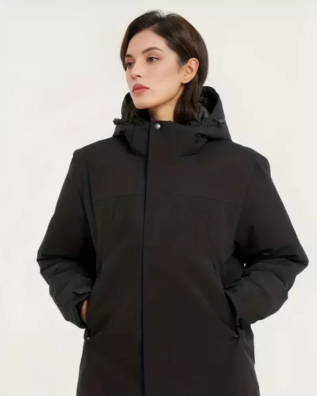 Une femme brune portant un blouson imperméable noir avec les mains dans les poches