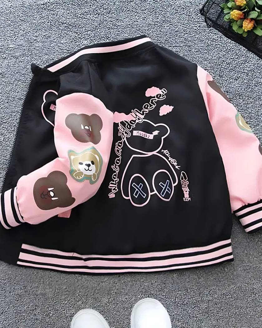 21777-w3vxrk-transformed Blouson teddy pour fille posรฉ de dos sur une moquette grise. Le blouson est ouvert, on voit lรฉgรจrement le cรดtรฉ gauche et la manche gauche est pliรฉ au niveau du coude. Le blouson est noir et les manches roses. Trois tรชtes d'oursons sur la manches gauche. Les contours d'un ourson et des inscriptions au ds du blouson. Un petit panier en mรฉtal noir en haut ร droite avec petites fleurs artificielles jaunes et vertes.