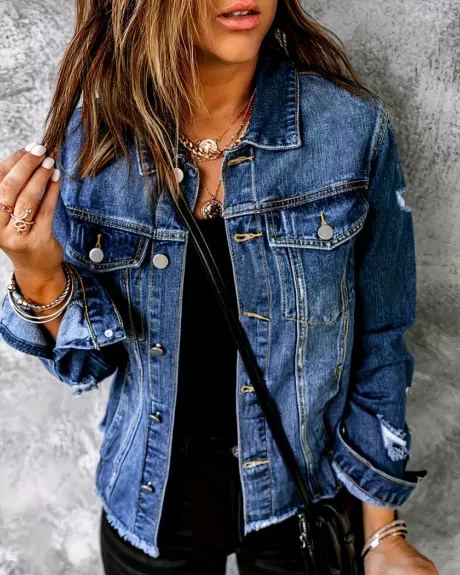 Une femme portant un blouson en jean déchiré sur les bras adossé à un mur gris