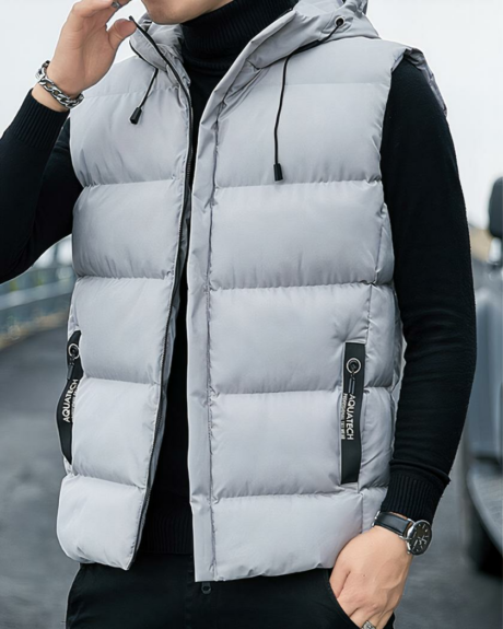 Un homme dans la rue portant un blouson sans manches à capuche gris avec les mains dans les poches de son pantalon