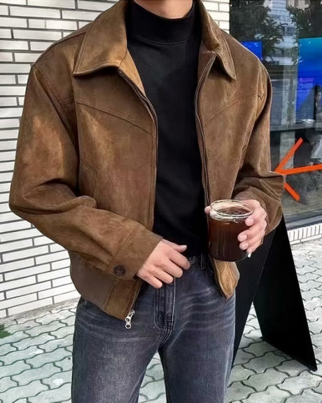 Un homme dans la rue portant un blouson style daim marron et portant un verre à la main gauche