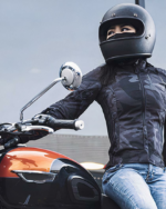 Une femme assise sur une moto avec un casque sur la tête portant un blouson de moto
