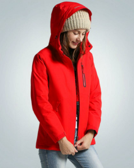 Une femme portant un blouson chauffant rouge avec la capuche sur la tête en train de fermer sa fermeture