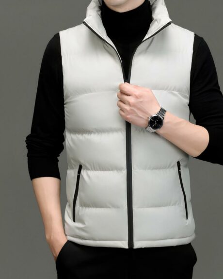 Homme de face dont on ne voit que le buste, portant un pull col roulé noir avec une doudoune sans manches gris clair