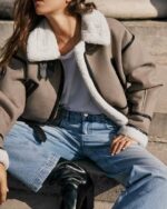 Une femme assise qui porte un blouson bombardier marron avec un col rabattu fourré