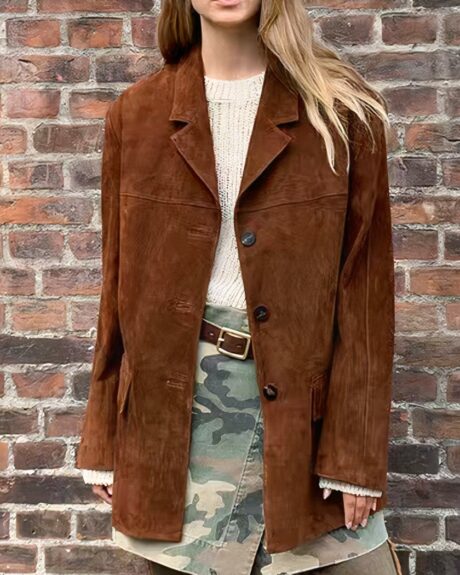 Une femme blonde portant un blouson vintage en daim marron, un mur en brique en arrière plan