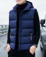 Un homme dans la rue portant un blouson sans manches à capuche bleu avec les mains dans les poches de son pantalon