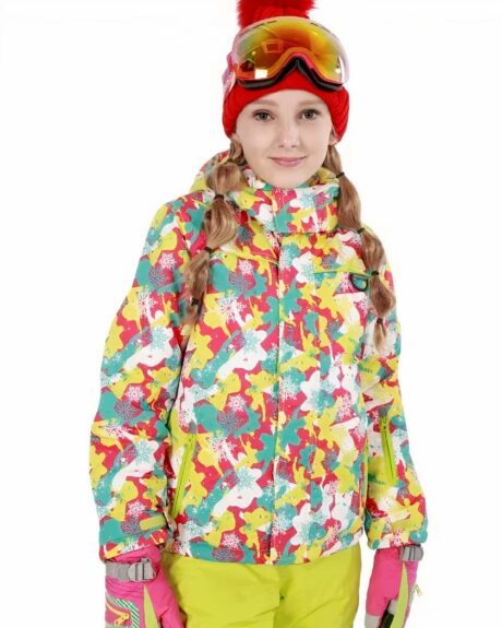 Fille avec cheveux blonds longs jusqu'à la poitrine, portant un bonnet rouge avec pompon, des lunettes de ski jaune, des gants de ski rose, un pantalon de ski jaune et un blouson de ki fermé jusqu'au col de couleurs mélangées : jaune, rose, bleu et blanc. Sur fond blanc.
