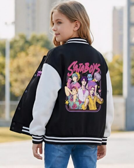 Une jeune fille de dos portant un blouson teddy enfant Kpop Demon Hunters Saja Boys noir et blanc avec un grand dessin coloré de groupe de musique dans le dos, sur un chemin ensoleillé à l'extérieur avec des arbres en arrière-plan.